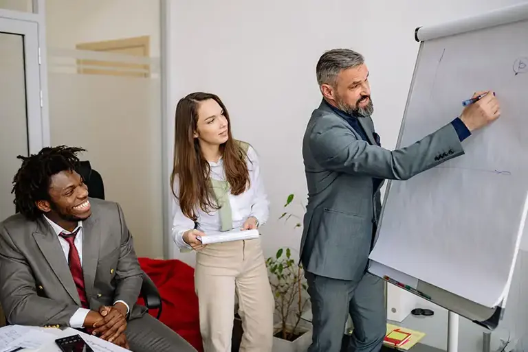 Three office workers are actively engaged writing on a whiteboard paper easel