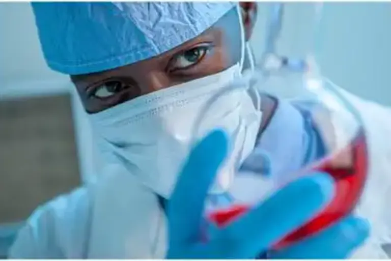 A masked scientist holds a chemical glass flask full of liquid