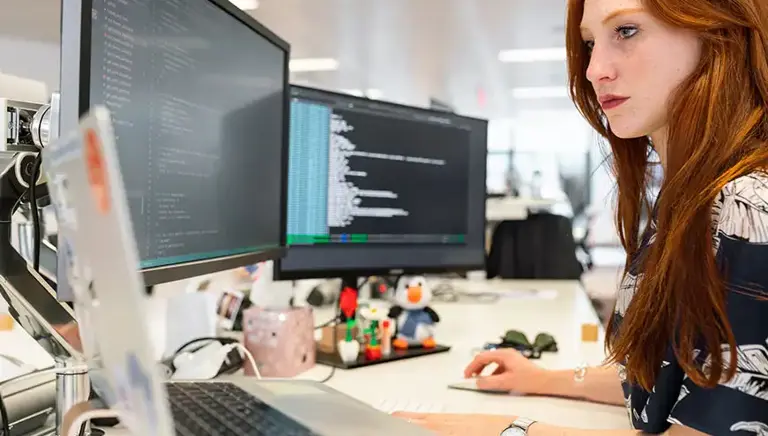 Office worker carefully looking over code across two screens 