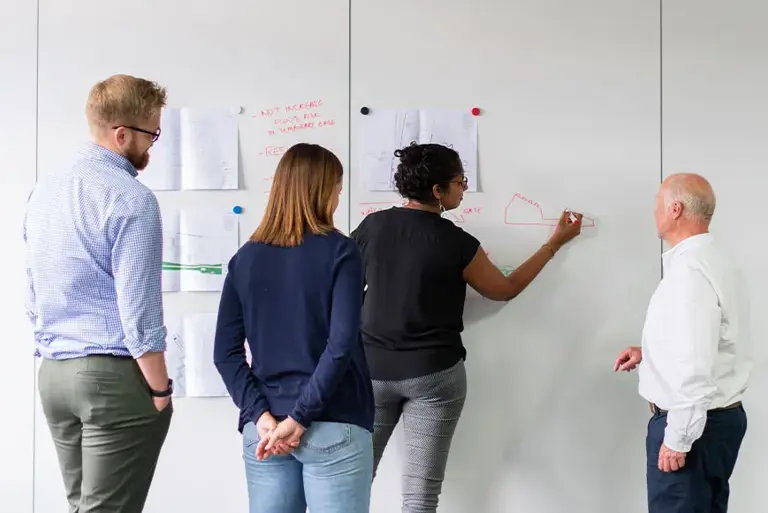 Four office workers drawing on sheets stuck on the wall 