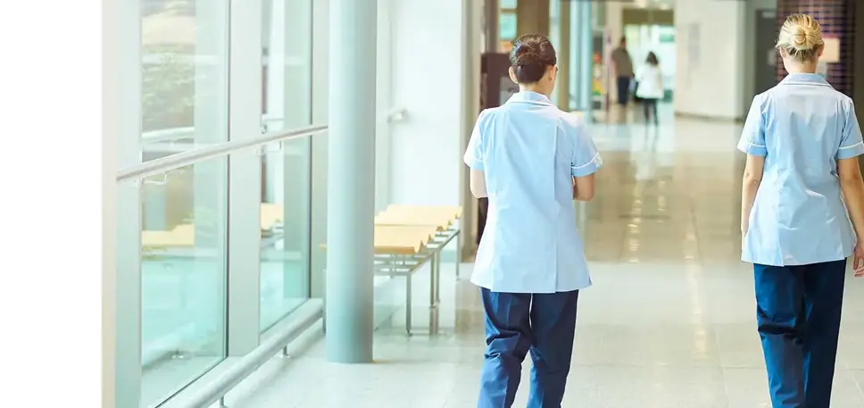 Three nurses, seen from behind, walk down a hospital corridor