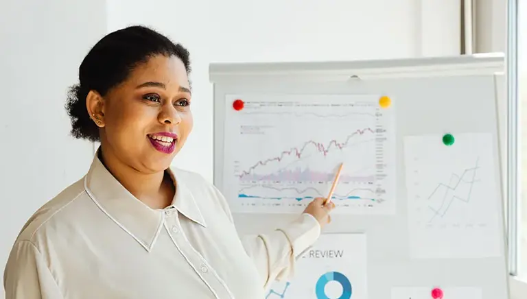 Office workers points to key charts on a whiteboard behind her