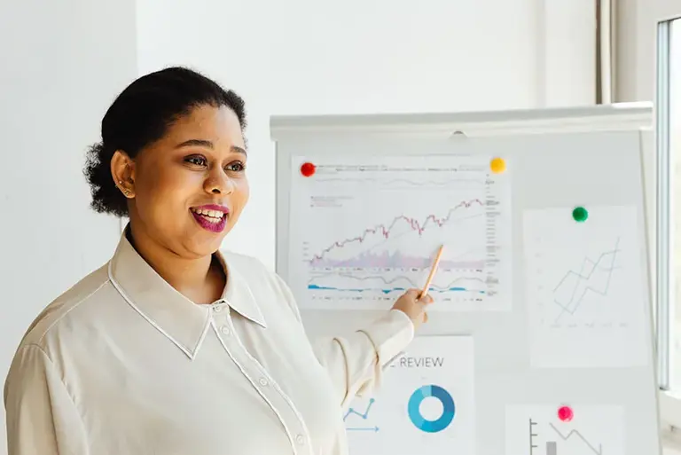 Office workers points to key charts on a whiteboard behind her