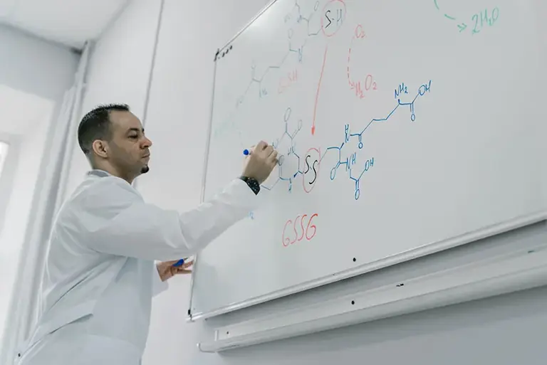 Scientist writes long molecular structures on a large wall mounted whiteboard 